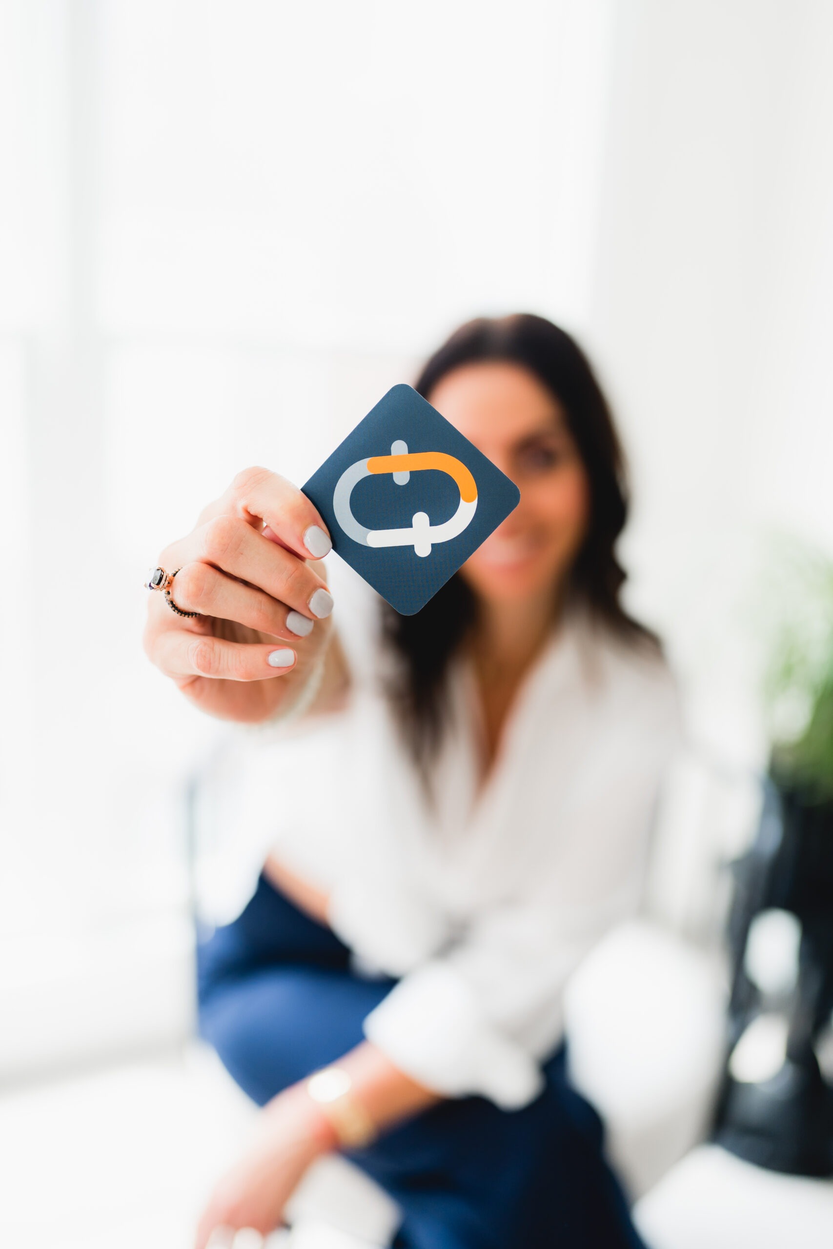 A woman holding a branded card with a distinctive logo, showcasing a modern workspace and emphasizing the card's significance.