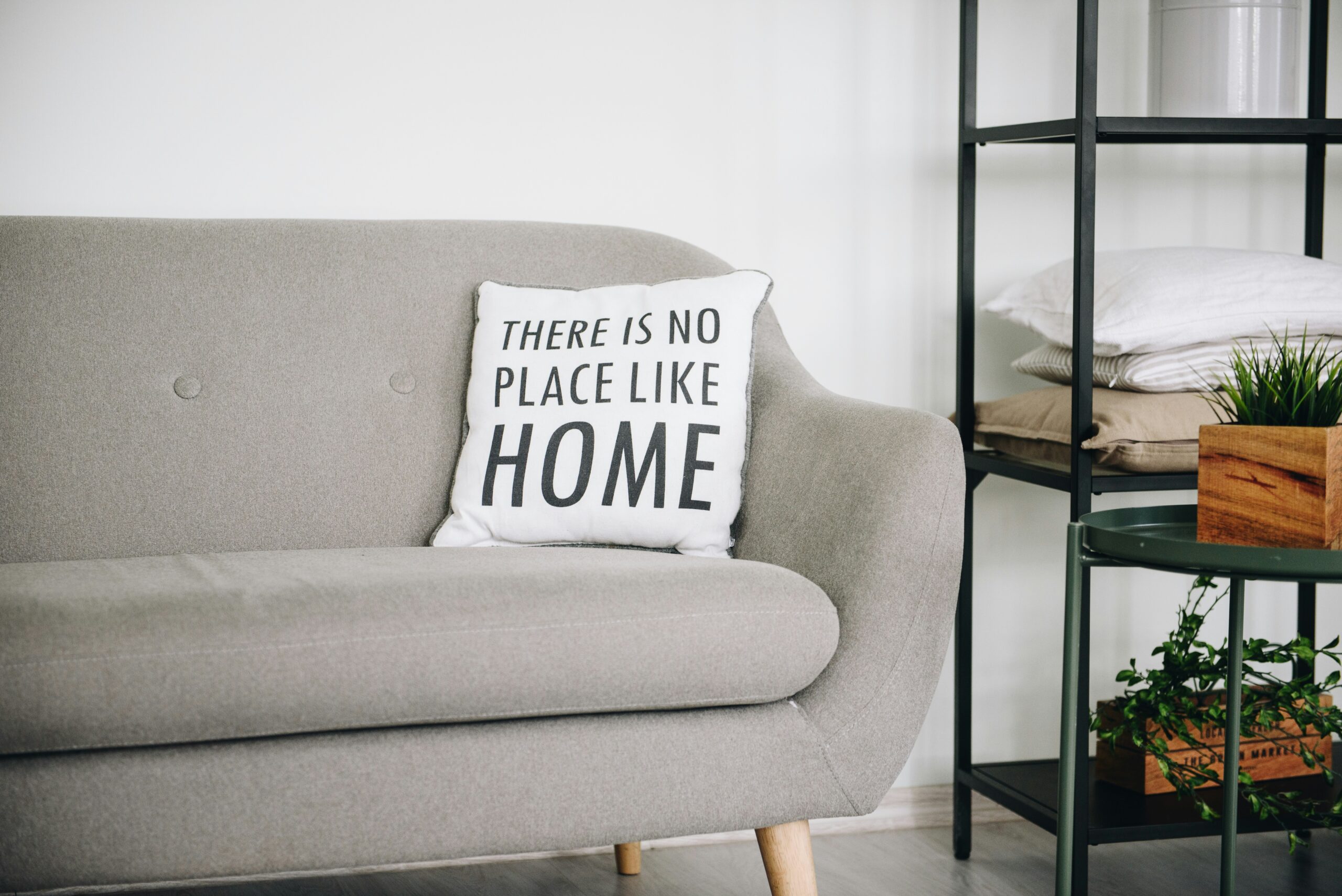 Cozy gray sofa adorned with a "There is no place like home" pillow, surrounded by minimal decor, emphasizing comfort and home aesthetics.