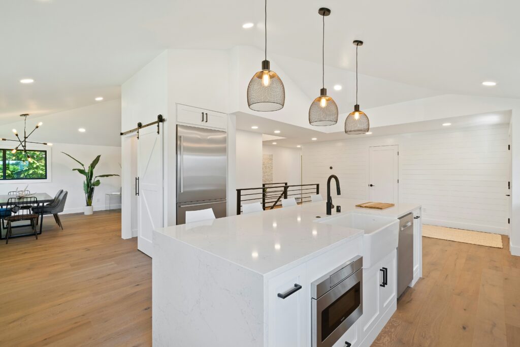 Modern kitchen with an island, featuring sleek cabinets, stainless steel appliances, and pendant lighting, opening to a dining area.