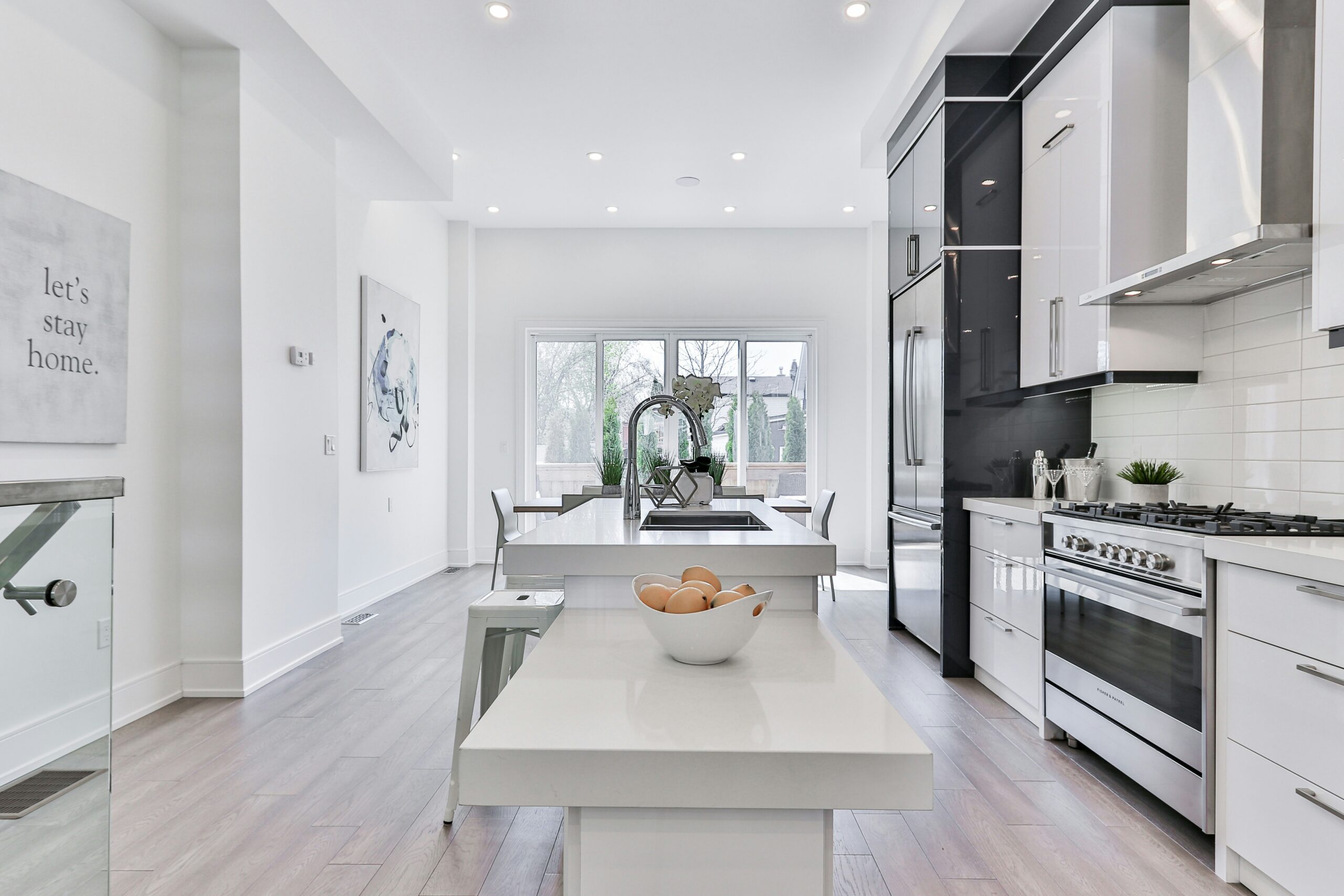 Modern kitchen featuring sleek white cabinetry, a large island with a bowl of eggs, and connecting dining area with a view of the outdoors.