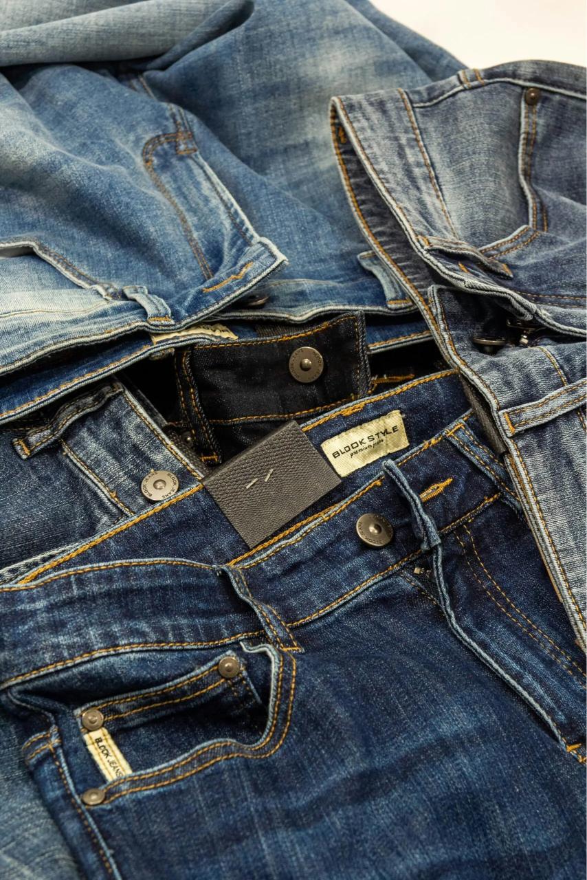 Assorted denim jeans in various shades of blue, layered and partially folded, highlighting their differing styles and textures.