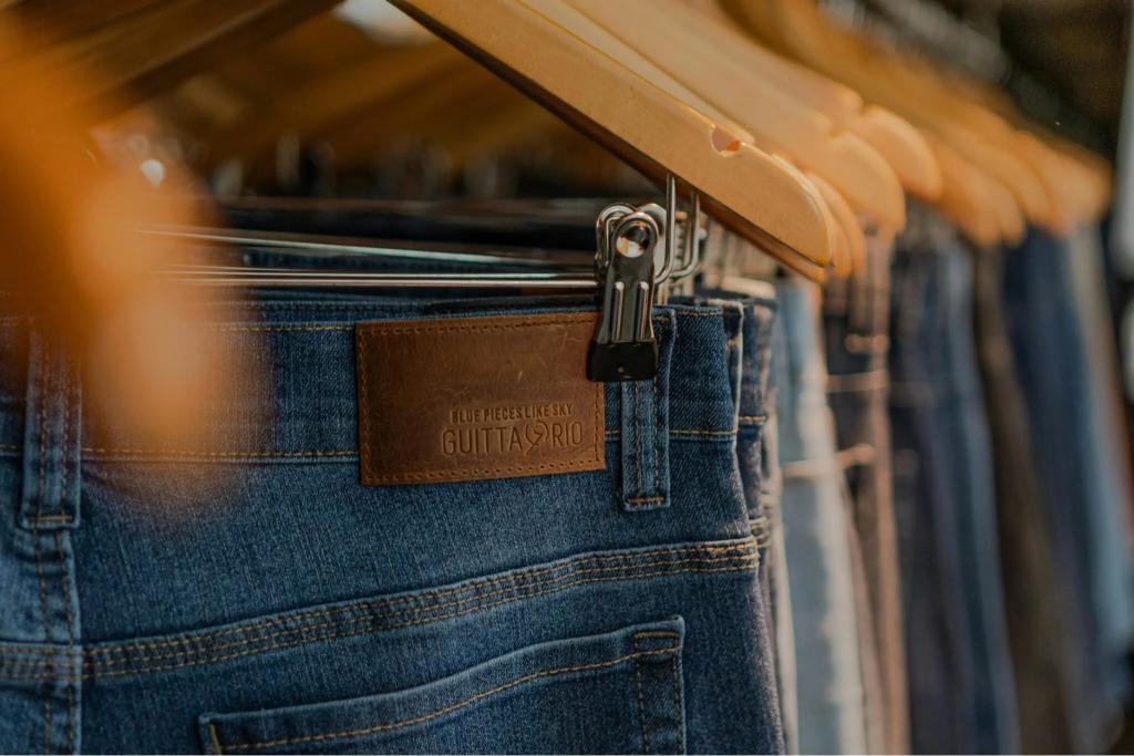 Hanging denim jeans with a brown leather label reading "Guttario" on a clothing rack. Showcases styles available for shoppers.
