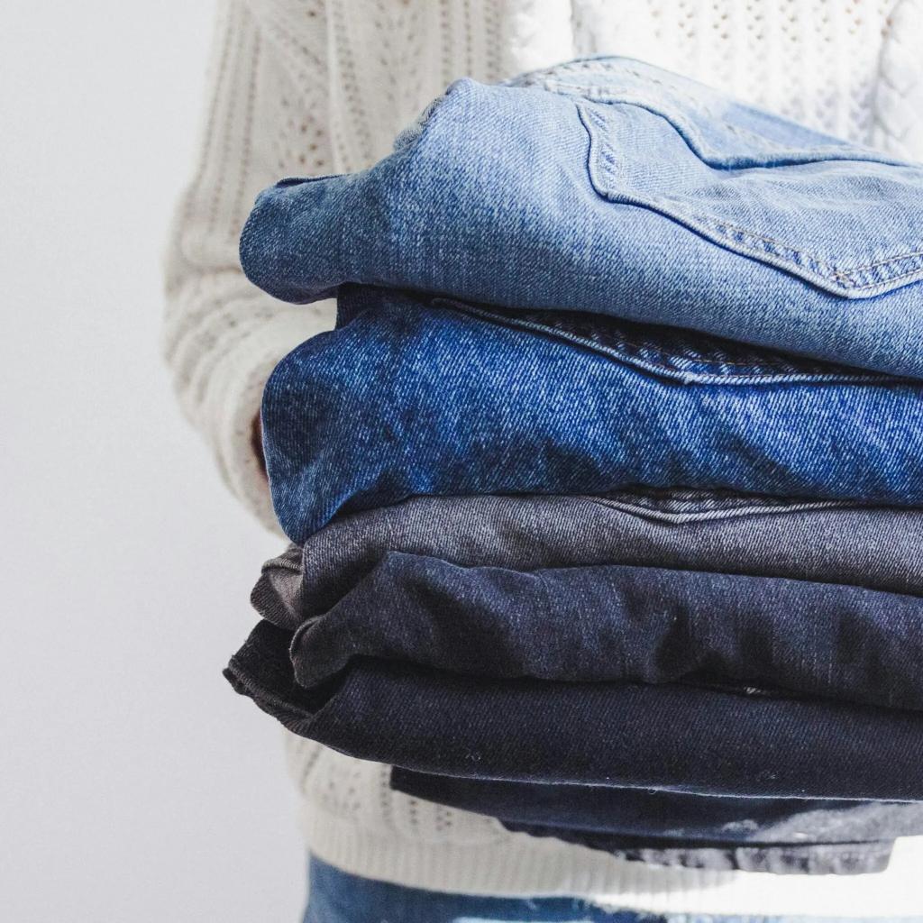 A person holds a stack of folded jeans in various shades of blue and black, emphasizing denim styles for fashion or wardrobe organization.